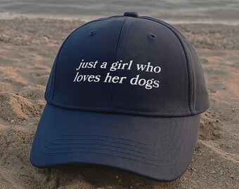 以下が含まれることがあります： 前面に「just a girl who loves her dogs」という白い刺繍テキストが施されたダークネイビーの野球帽。この帽子は構造化されたクラウン、目に見えるステッチが施されたカーブしたつば、そして中央上部にボタンが付いています。