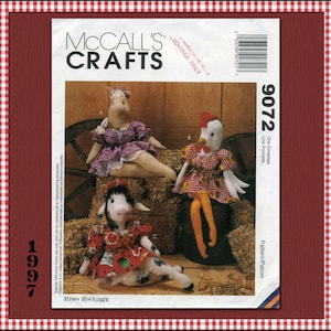 May include: A McCall's Crafts 9072 sewing pattern envelope featuring three stuffed animal dolls: a horse in a purple floral dress, a chicken in a sunflower print dress with orange tights, and a cow in a red watermelon print dress.