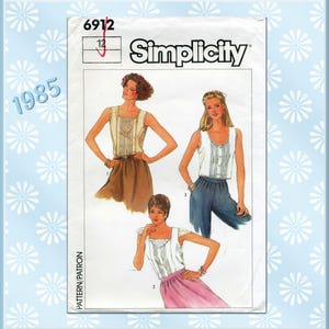 May include: A Simplicity sewing pattern envelope numbered 6912 for size 12, dated 1985. The illustration displays three variations of a sleeveless top with a square neckline, vertical pleats, and lace trim, paired with a skirt or trousers.