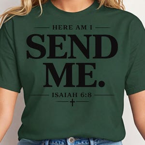 Op de afbeelding: Een donker bosgroen T-shirt met korte mouwen en zwarte tekst die HERE AM I SEND ME leest. Onder de tekst toont het T-shirt ISAIAH 6:8 met een klein kruissymbool gecentreerd tussen twee horizontale lijnen, wat een grafisch ontwerp vormt.