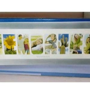 May include: A rectangular Davco brand photo frame in a blue box. The frame features the word MEMORIES spelled out with individual photo slots containing images of a sunflower, people, a cactus, and landscapes, set against a white background.