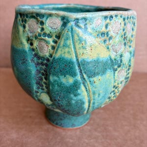 May include: A ceramic cup featuring a vibrant teal and lime green glaze with a textured surface. The exterior displays raised petal-like vertical ridges and a pattern of small, circular indentations filled with a light beige, speckled finish.