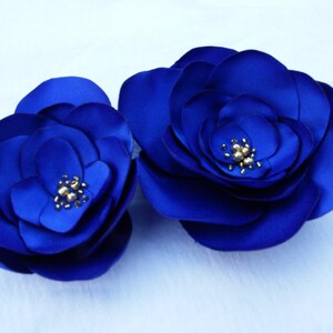 May include: Two large, blue satin fabric flowers with gold centers. The flowers are layered and have a three-dimensional appearance.