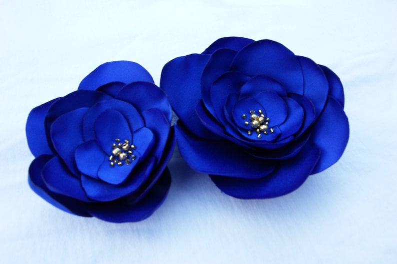 May include: Two large, blue satin fabric flowers with gold centers. The flowers are layered and have a three-dimensional appearance.