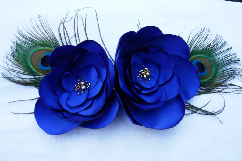 May include: Two large blue satin flowers with gold accents, each with a peacock feather on either side.