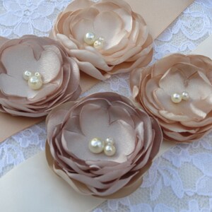 May include: A satin ribbon sash with four blush-colored fabric flowers, each with pearl embellishments.