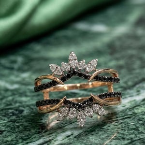Könnte beinhalten: Ein Ring-Guard aus Roségold mit zwei geschwungenen Bändern, die durch einen Steg verbunden sind. Das Design ist mit kleinen, runden schwarzen Steinen entlang der Bänder und einer Reihe von weißen Marquise- und Rundsteinen in Kronenform verziert.