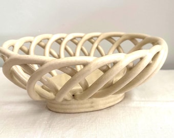 May include: A cream-colored ceramic bowl featuring an openwork lattice design. The structure is composed of interconnected, rounded clay strips that form a woven, basket-like pattern, resting on a solid, circular base with a smooth, matte finish.