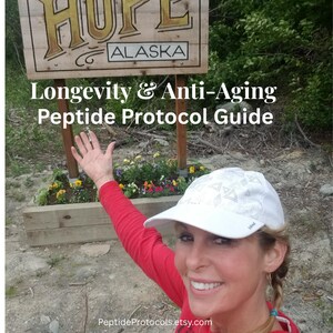 May include: A white baseball cap with a geometric pattern worn by a person in a red long-sleeved shirt. In the background, a wooden sign reads HOPE ALASKA above a flower bed. Text overlay reads Longevity & Anti-Aging Peptide Protocol Guide.