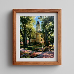 May include: A framed print depicting a yellow historic building with a clock tower, surrounded by lush green trees and vibrant flower beds. A black metal lamp post and wooden park benches are situated along a brick walkway in the foreground.
