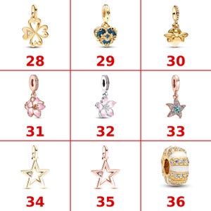 K&ouml;nnte beinhalten: Eine Sammlung von neun Schmuckanh&auml;ngern, nummeriert von 28 bis 36. Die Anh&auml;nger umfassen ein goldenes Kleeblatt, ein blaues Herz, eine goldene Biene, zwei rosa Blumenmotive, einen Seestern, zwei Sternumrisse und eine wei&szlig;-gold gestreifte Perle.
