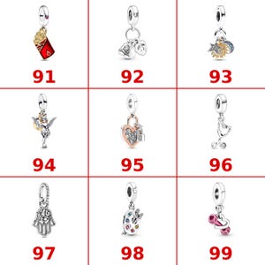 K&ouml;nnte beinhalten: Eine Sammlung von neun silberfarbenen Metallanh&auml;ngern, nummeriert von 91 bis 99. Die Motive umfassen eine rote Pommes-Frites-Schachtel, Babyartikel, Himmelsk&ouml;rper, einen Amor, ein Herz-Vorh&auml;ngeschloss, ein Stethoskop, eine Hamsa-Hand, eine Farbpalette.