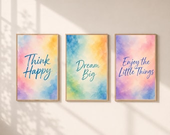 May include: A set of three rectangular wall art prints in light wooden frames. Each print features a vibrant watercolor background in shades of pink, yellow, blue, and green. The text reads Think Happy, Dream Big, and Enjoy the Little Things.