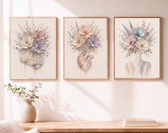 May include: A set of three framed wall art prints featuring watercolor illustrations. The first shows a human brain, the second an anatomical heart, and the third a human silhouette, each topped with a bouquet of pastel flowers in soft pink, blue, and purple tones with dripping paint effects.