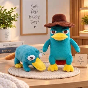 Op de afbeelding: Twee pluche vogelbekdier-speeltjes. Eén staat rechtop met een bruine fedora-hoed, met een blauwgroen lichaam, gele snavel en gele voeten. De tweede staat op vier poten, ook blauwgroen met een gele snavel en witte ogen met zwarte pupillen.