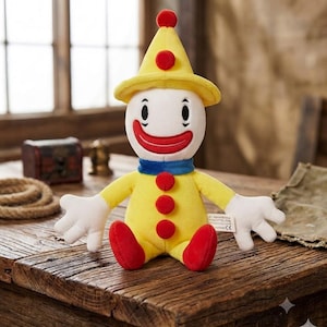 May include: A plush clown doll featuring a yellow hat with a red pom-pom, a white face with a wide red smile, a blue neck collar, and a yellow body decorated with three red buttons. The doll has white hands and red feet, with a small white tag.