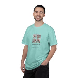 May include: A light turquoise short-sleeve t-shirt featuring a red square stamp graphic with Chinese characters. Below the stamp, the text reads: Tranquility Leads Far, followed by smaller text including the phrase to good and far-reaching goals.