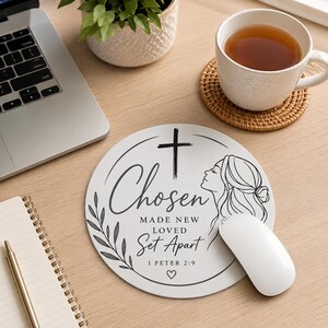 May include: A round white mouse pad featuring a black line art illustration of a profile of a person, a cross, and a leafy branch. The text reads: Chosen, MADE NEW, LOVED, Set Apart, 1 PETER 2:9, and includes a small heart symbol at the bottom.