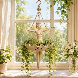 May include: A hanging planter featuring a cream-coloured ballerina figurine with arms outstretched. The figure holds a scalloped bowl filled with green trailing vines. The word Text is printed on the front of the bowl, which is suspended by gold-toned chains from a central hook.
