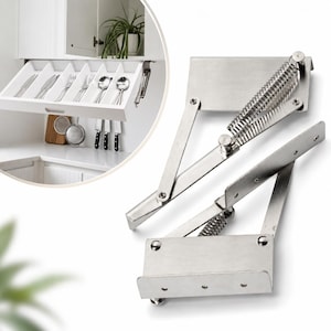May include: Two silver-coloured metal cabinet hinges with integrated springs, designed for lift-up doors. The mechanism features flat mounting plates and articulated arms. An inset shows the hardware installed on a white kitchen cabinet drawer.