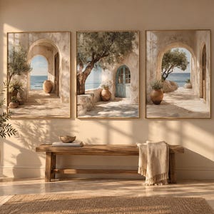 May include: A triptych of framed wall art prints depicting Mediterranean coastal scenes with stone archways, olive trees, terracotta pots, and blue doors overlooking the sea. The artwork features warm, neutral tones and light-filled architectural details.