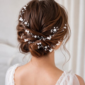 May include: A flexible hair vine accessory featuring delicate silver-toned wire, small white floral accents, and tiny round white pearls. The decorative piece is woven through a styled updo, creating a layered look with multiple branching stems.
