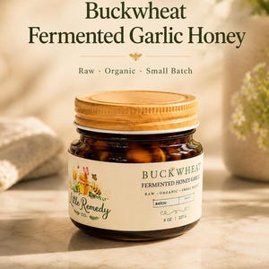 May include: A glass jar of Buckwheat Fermented Garlic Honey with a wooden lid. The label features the text Little Remedy Co., Buckwheat Fermented Honey Garlic, Raw, Organic, Small Batch, and 8 oz | 227 g, along with illustrations of a bee and honey.