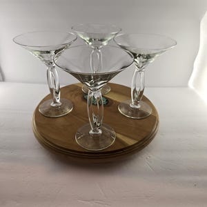 May include: Four clear glass martini glasses with wide, conical bowls and stems featuring a distinctive twisted, open-loop design. The glasses are arranged in a cluster, each resting on a circular base, showcasing a transparent, smooth finish.