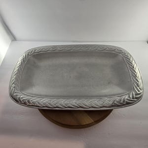 May include: A rectangular silver-toned metal serving tray featuring a textured, braided wheat pattern along the raised border. The center of the tray is smooth with a matte finish, and the overall design has a metallic, slightly weathered appearance.