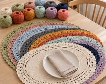May include: A collection of oval crochet placemats in various colors including cream, green, orange, blue, grey, and purple, stacked on top of each other. A white ceramic plate with a folded beige linen napkin sits on the top cream placemat.