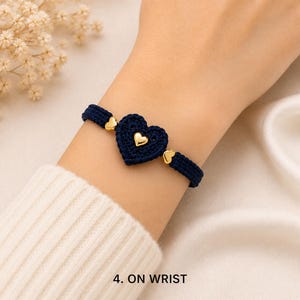 May include: A dark blue woven cord bracelet featuring a central crocheted heart charm and two smaller gold-toned heart accents. The bracelet is secured with a matching dark blue cord band. The text 4. ON WRIST is visible at the bottom.