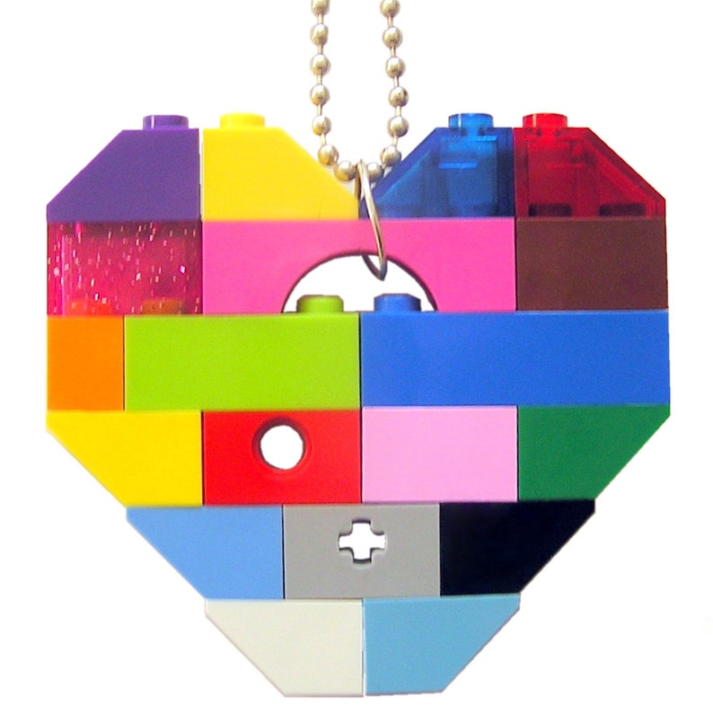 May include: A colorful heart-shaped pendant made of LEGO bricks. The pendant is strung on a silver chain and features a variety of colors, including red, blue, green, yellow, pink, purple, and orange.