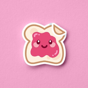 May include: A die-cut sticker of a slice of white bread topped with a thick layer of bright pink jam. The jam features a smiling face with two dark eyes, a small curved mouth, and rosy cheeks. The top right corner of the bread is slightly peeled back.