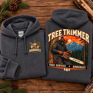 Op de afbeelding: Een donkergrijze hoodie met een afbeelding van een boomverzorger met een kettingzaag, bergen en bomen. De achterkant toont de tekst TREE TRIMMER, TREE SERVICE en ARBORIST. Op de borst staat een kleiner logo van een boomverzorger.