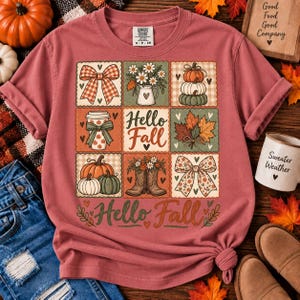 May include: A dusty rose short-sleeve t-shirt featuring a grid of nine squares with autumn-themed illustrations including pumpkins, a coffee cup, flowers, boots, and bows. The text "Hello Fall" is printed in the center square and at the bottom.