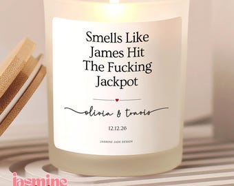 May include: A frosted glass candle with a white label featuring the black text Smells Like James Hit The Fucking Jackpot, a small red heart, the names olivia & travis in script, the date 12.12.26, and the text JASMINE JADE DESIGN at the bottom.