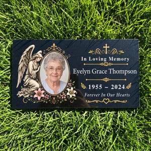 Peut inclure: Une plaque commémorative rectangulaire en granit noir avec le portrait d'une femme âgée dans un cadre ovale, une illustration d'ange et le texte doré In Loving Memory, Evelyn Grace Thompson, 1955-2024, et Forever In Our Hearts.