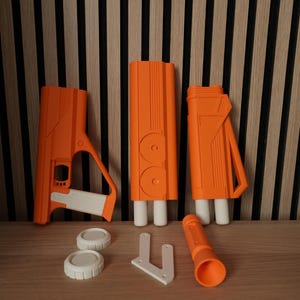 Puede incluir: Un conjunto de componentes de juguete tipo bláster de plástico naranja y blanco, que incluye tres secciones principales del cuerpo, dos tapas blancas circulares, un soporte angular blanco y una extensión de cañón cilíndrica naranja.