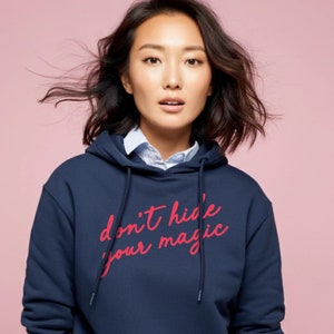 May include: A navy blue hooded sweatshirt with the phrase "don't hide your magic" printed in pink on the front.