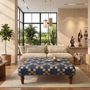 Könnte beinhalten: Ein großer quadratischer Hocker mit einem geometrischen Muster in Blau, Creme und Gold, der auf vier dunkelbraunen, gedrechselten Holzbeinen steht und zentral in einem Wohnzimmer auf einem hellen Teppich platziert ist.