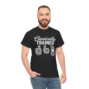 Może przedstawiać: Czarny t-shirt z krótkim rękawem z białym napisem Classically Trained nad grafiką przedstawiającą trzy metalowe pedały samochodowe, w tym sprzęgło, hamulec i gaz, ułożone w układzie typowym dla manualnej skrzyni biegów.