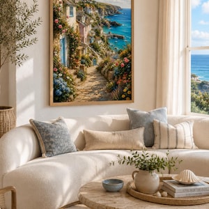 May include: A framed wall art print depicting a coastal village scene with stone cottages, a winding path, and vibrant flowers overlooking a blue ocean under a bright sky. The artwork features a palette of blues, greens, pinks, and earthy stone tones.