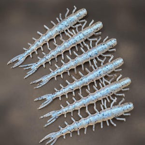 May include: A set of six translucent light blue fishing lures shaped like centipedes, each featuring a segmented body with multiple thin legs, a forked tail, and small black speckles distributed across the entire surface of the lure.