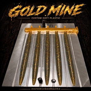 May include: A metal injection mold containing five long, slender, ribbed soft plastic fishing lures with gold glitter. The text GOLD MINE CUSTOM SOFT PLASTIC appears at the top, and corewickedbaits is printed at the bottom of the mold.