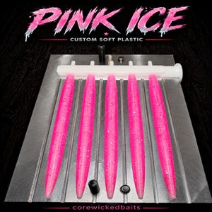 May include: A metal injection mold for fishing lures featuring five cavities filled with bright pink, glitter-infused soft plastic bait. The top of the mold displays the text PINK ICE CUSTOM SOFT PLASTIC and the bottom shows corewickedbaits.
