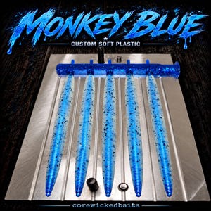 May include: A metal injection mold for fishing lures featuring five parallel cavities filled with translucent blue soft plastic baits containing black glitter flecks. The text MONKEY BLUE CUSTOM SOFT PLASTIC and corewickedbaits is visible.