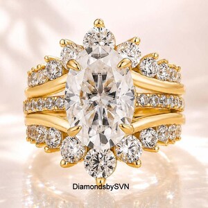 Peut inclure: Une bague en or avec une grande pierre centrale ovale transparente entourée d'un halo de pierres rondes transparentes plus petites. L'anneau se compose de plusieurs couches dorées ornées de pierres rondes. Le texte indique DiamondsbySVN.