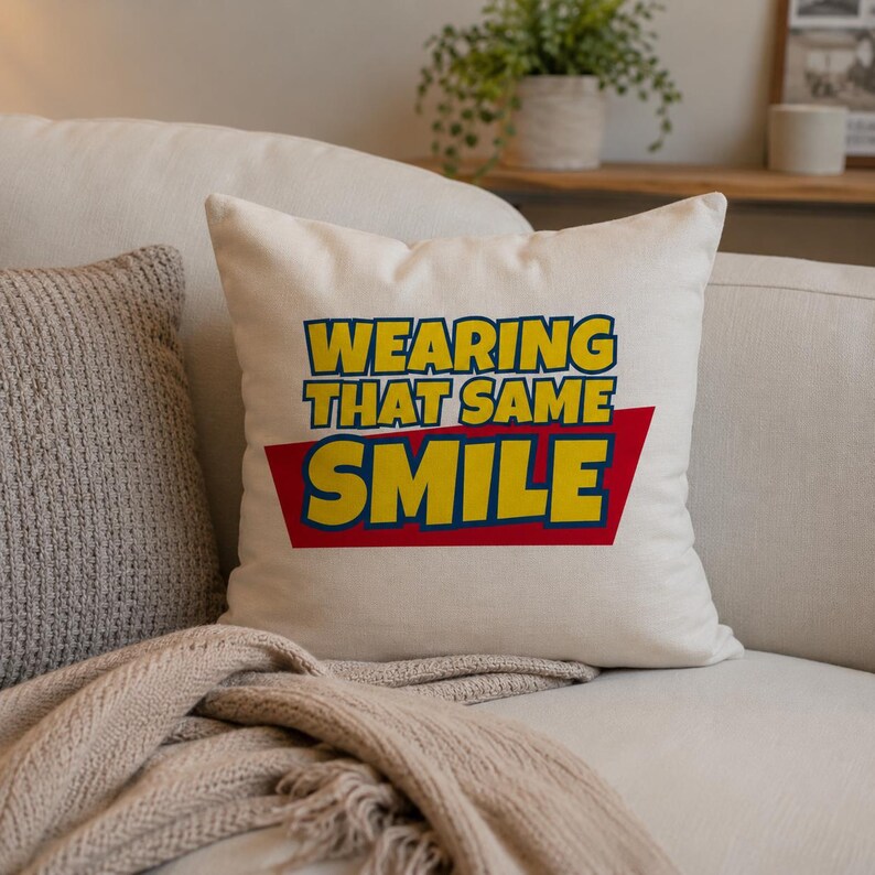 Peut inclure: Un coussin carr&eacute; blanc cass&eacute; avec le texte WEARING THAT SAME SMILE en lettres jaunes grasses. Le mot SMILE est plac&eacute; sur un fond trap&eacute;zo&iuml;dal rouge uni. Le coussin pr&eacute;sente une texture de tissu lisse et unie ainsi qu'un design simple et &eacute;pur&eacute;.