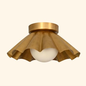 May include: A flush mount ceiling light fixture featuring a wide, scalloped brass shade with a metallic gold finish. A single, spherical white glass globe bulb is centered within the shade, extending slightly below the bottom edge of the metal.