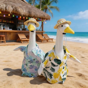 May include: Two white goose figurines standing on sand, each wearing a straw hat and a short-sleeved button-down shirt. One shirt features a blue and purple leaf pattern, while the other has a yellow and green leaf pattern with a daisy on the hat.